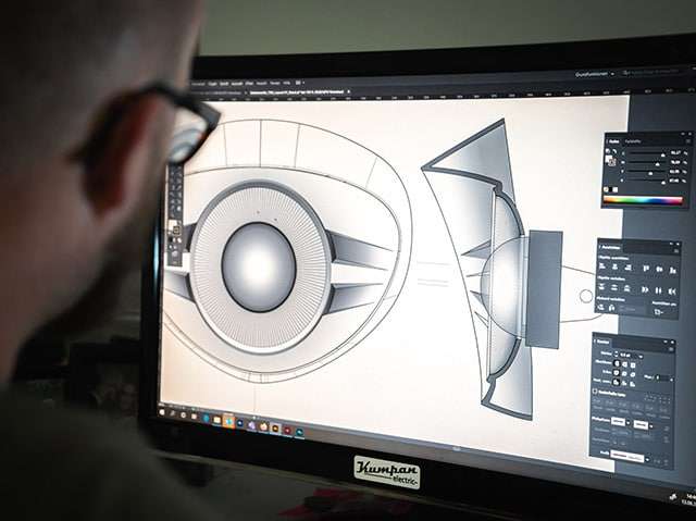 Designer working on CAD software with a detailed drawing of a speaker on the monitor in a tech design studio.