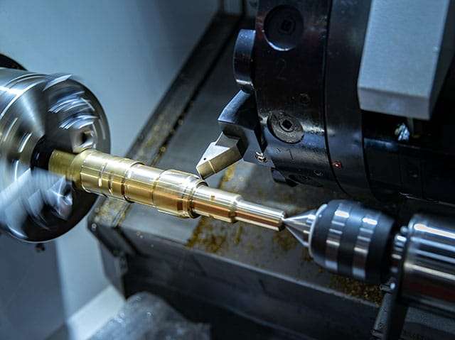 Precision metal manufacturing with a lathe machine cutting brass component in a workshop.